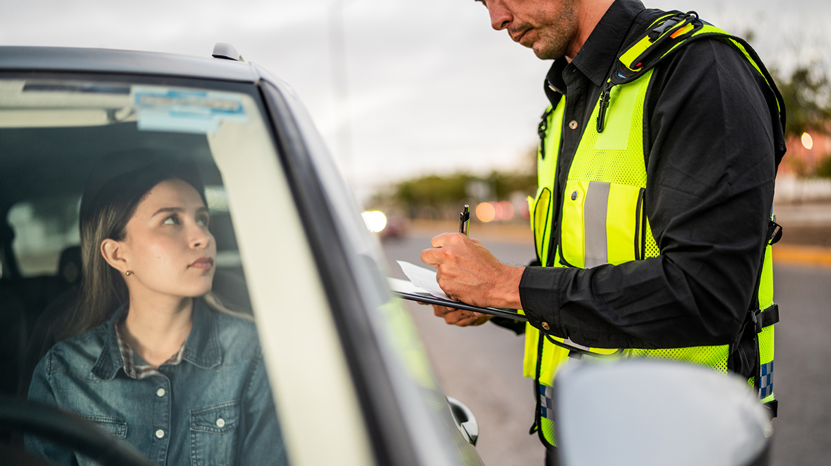 Woman recieving a traffic ticket from a police office while sitting in her vehicle