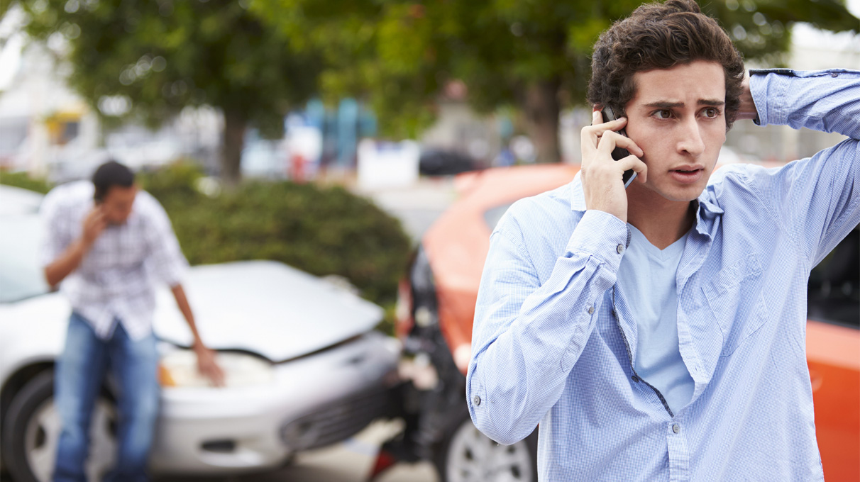 Man on the phone with a two vehicle accident behind him