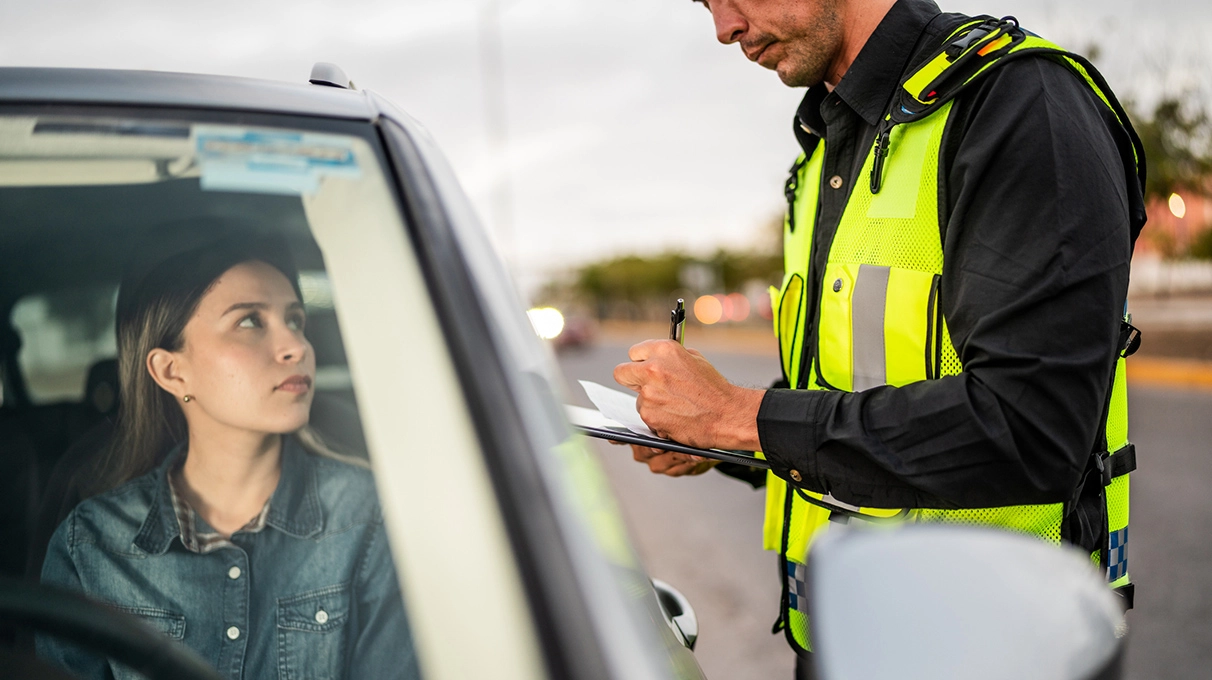 Woman receiving a traffic ticket from a police office while sitting in her vehicle